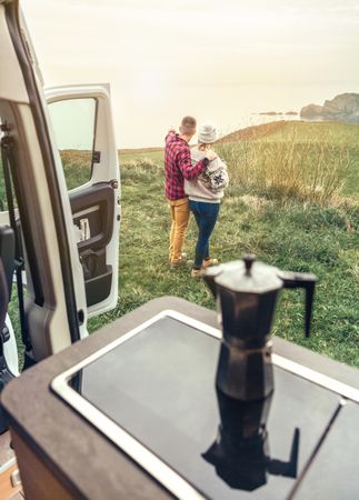 Couple enjoying beautiful morning view outside of camper van with cup of coffee, vertical