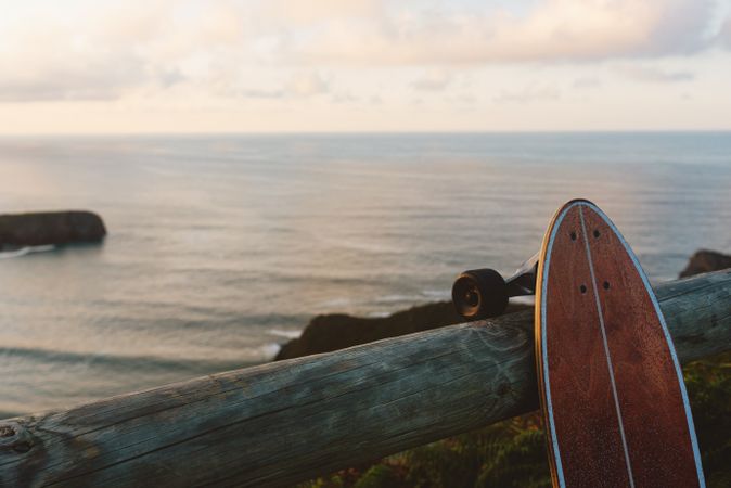 Surf skate leaning on wooden railing against blurred beach