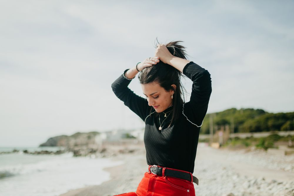stylish woman holding her hair and looking down in calm sea