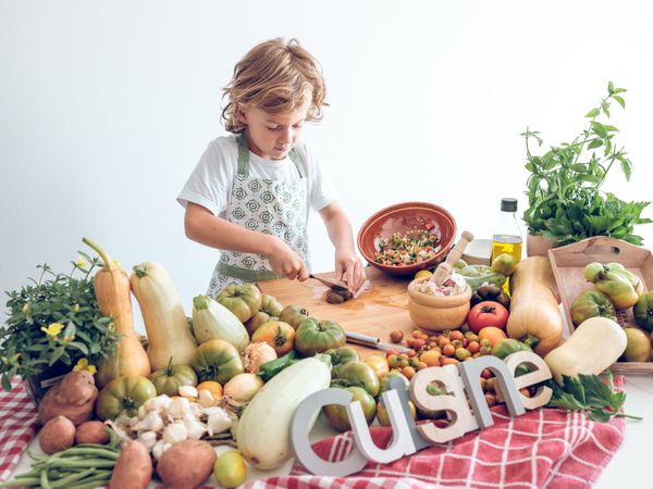 Positive preteen boy cutting vegetables on wooden board while cooking
