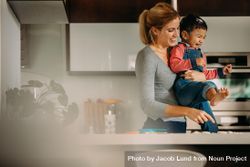 Smiling woman holding his son in her arms while making cookies in kitchen 0yzQG5