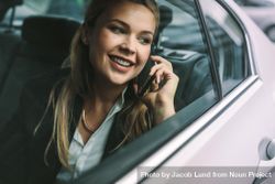 Smiling young businesswoman talking on the cell phone while sitting in back seat of a cab 5QxDN0
