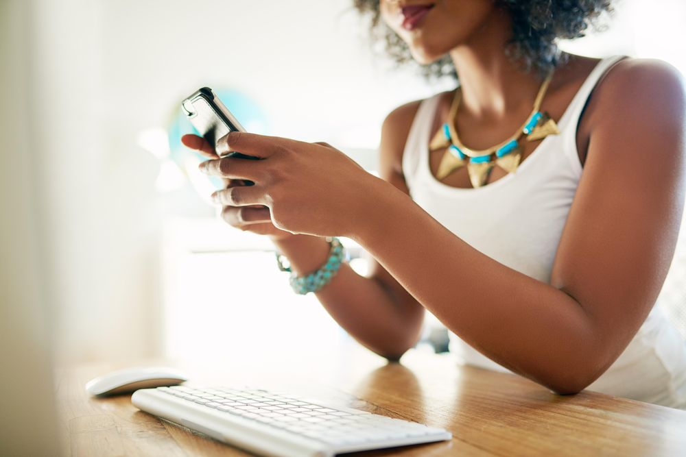 Stylish Black woman in vest texting at desk