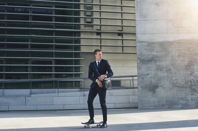 Professionally dressed businessman skateboarding with leather computer bag