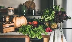 Assortment of vegetables, squash, tomatoes, radishes, herbs, on rustic kitchen counter