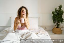 Woman yawning as she sips her coffee in bed 5oDQ6g