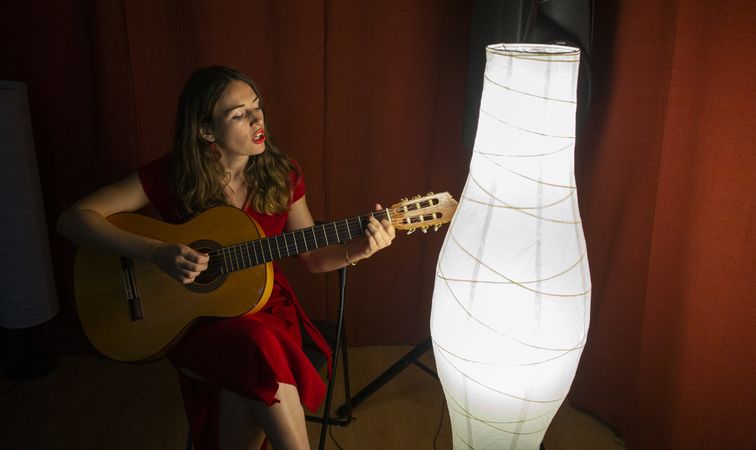 Woman singing and playing guitar on stage in lamplight