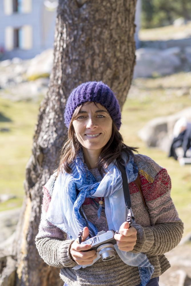 Female in woolen hat and sweater looking up while holding camera in front of tree