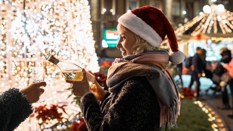 Young woman in a Santa hat pouring champagne into a glass at a Christmas market.