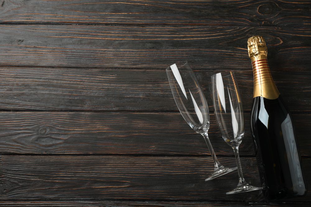 Champagne glasses and bottle on wooden background, space for text