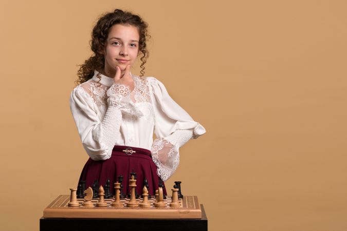 Young girl confidently smiling while considering chess move.