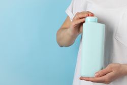 Woman holds blank shampoo bottle on blue background, space for text