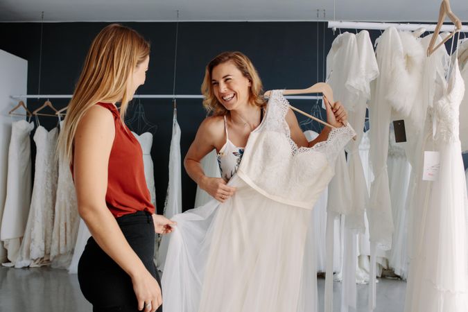 Wedding fashion store assistant helps the bride in choosing bridal dress
