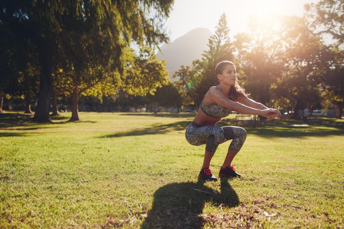 Full length shot of young woman practicing squats in park