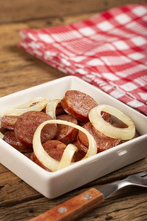 Sliced calabrese sausage with onion on wooden background.