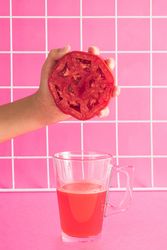 Hand holding half of red tomato and squeezing in glass