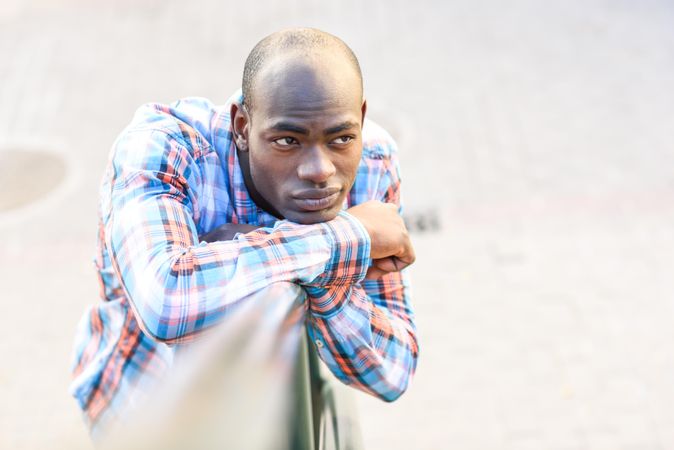 Picture of male in plaid shirt leaning on railing with listless expression