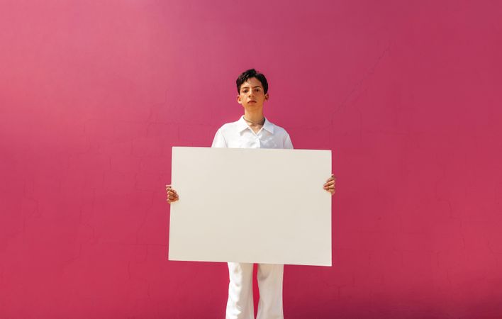Young male activist holding a blank banner against a pink background