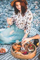 Woman holding wine glass with plate of sliced orange and tray of breads and meats