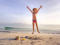 Happy boy raising arms and jumping on sandy beach