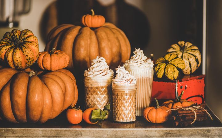 Three frothy drinks with whipped cream topping on table among decorative squashes