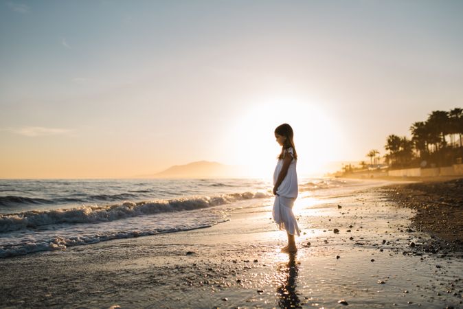 Adorable girl walking on seaside at sunset