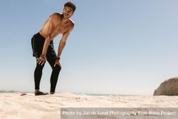 Fit male bending down to his knees after workout on a beach 0v1edb