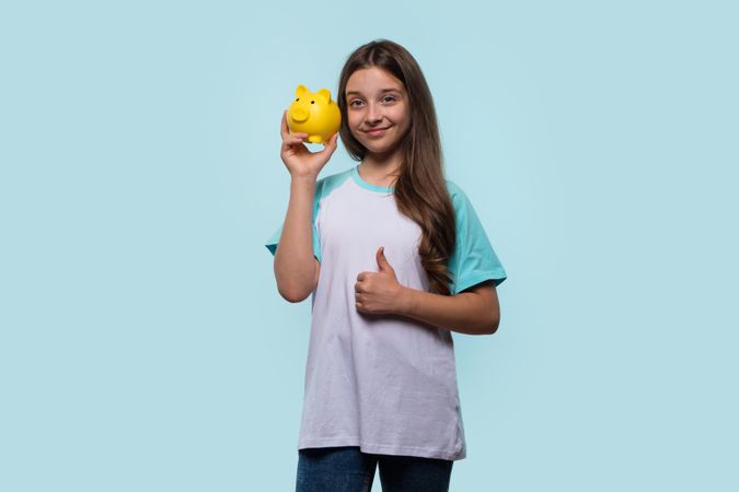 Girl holds yellow piggy bank and gives thumbs up