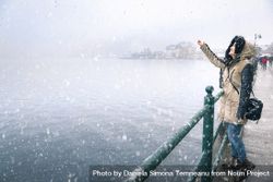 Woman reaching for snowflakes on a snowy day by a lake 0LWzVb
