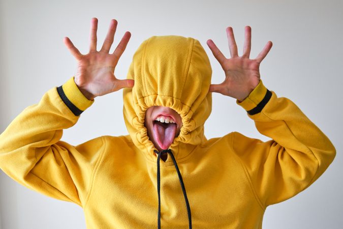 Anonymous child in hoodie mocking on gray backdrop