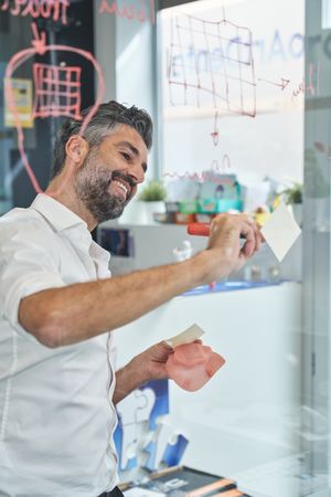 Cheerful worker with respirator writing on glass wall