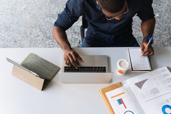 Black male writing in notepad near laptop in office
