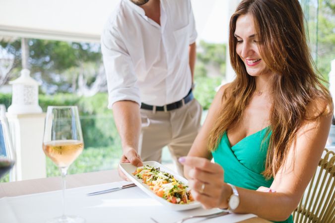 Crop waiter serving salad for woman in restaurant