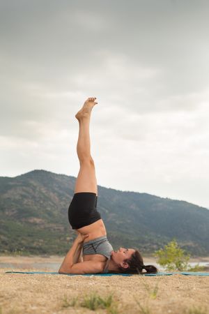 Woman practicing yoga outdoors near water
