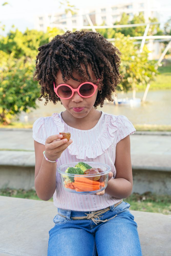 Little girl eating healthy food in a park. Family lifestyle concept.