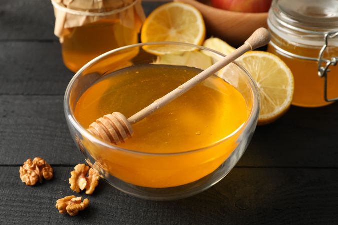 Bowl with honey, dipper and walnut on wooden background, close up
