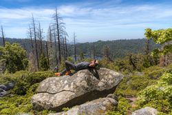 Relaxed hiker resting on big rock in forest