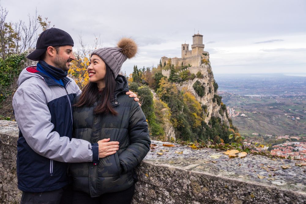 Lovely cheerful multiracial couple bonding near by stony fence viewing on castle on hill