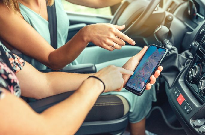 Close up side view of woman driving a motorhome checking map on phone with friend