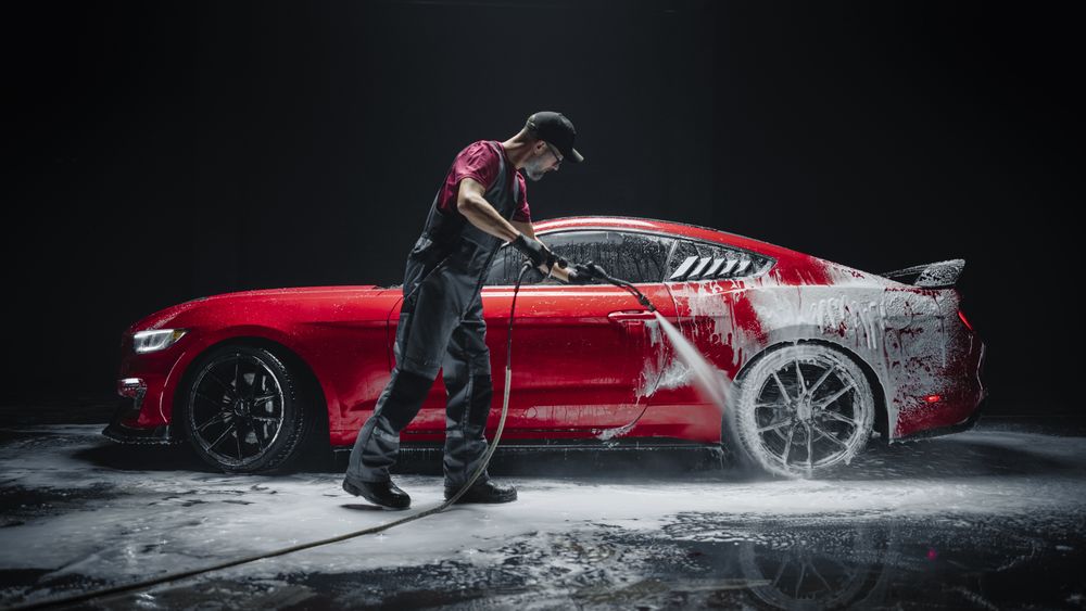 Car Wash Expert Using Water Pressure Washer to Clean a Red Modern Sportscar.