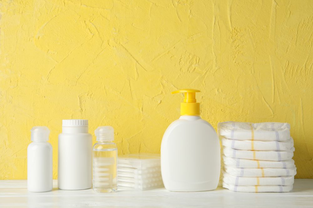 Baby hygiene accessories on wooden table against yellow background