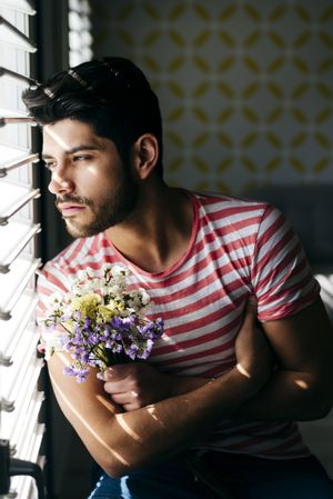 Young sad man with flowers looking out window