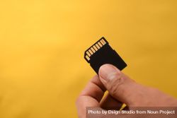 Hand holding SD card for data with yellow background with copy space 4NEmPA