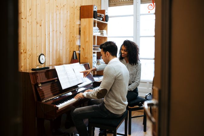 Man playing piano near woman teacher in studio