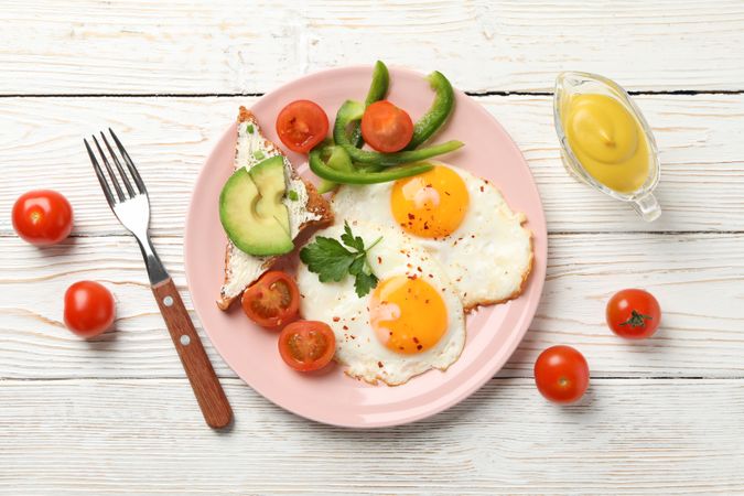 Breakfast of eggs, avocado and tomatoes on pink plate