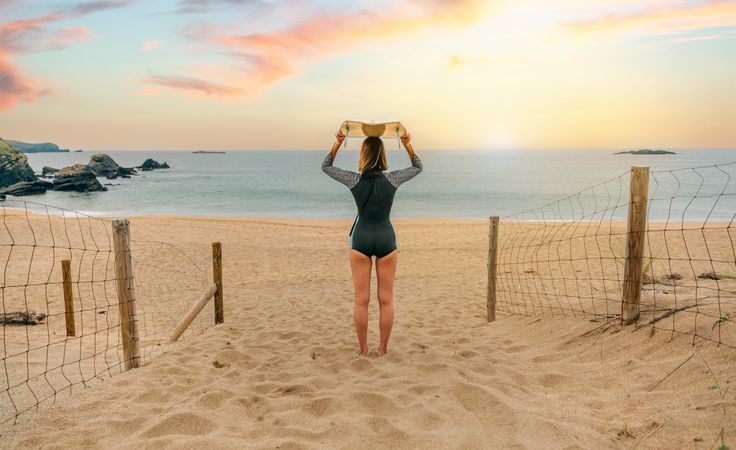 Woman balancing surfboard on her head while enjoying beautiful view of beach