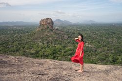 Tourist against solitary rock in middle of green forested plain under clear sky in summer