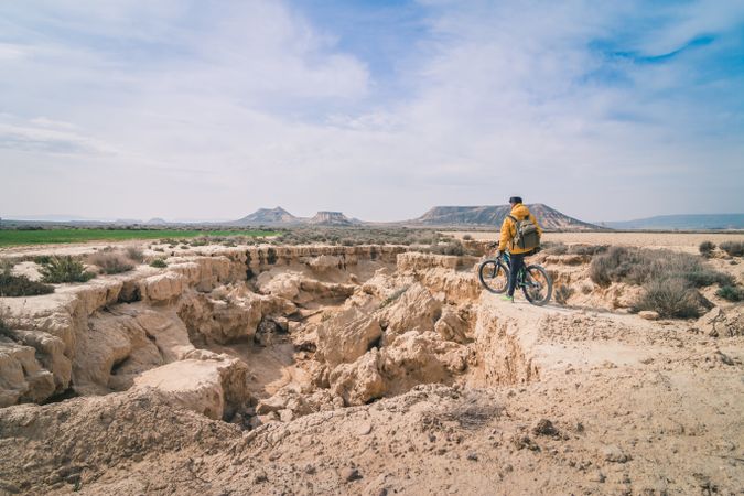 Man with bicycle standing on stone in desert hills