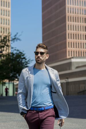 Serious man with sunglasses walking with hand on pocket outside