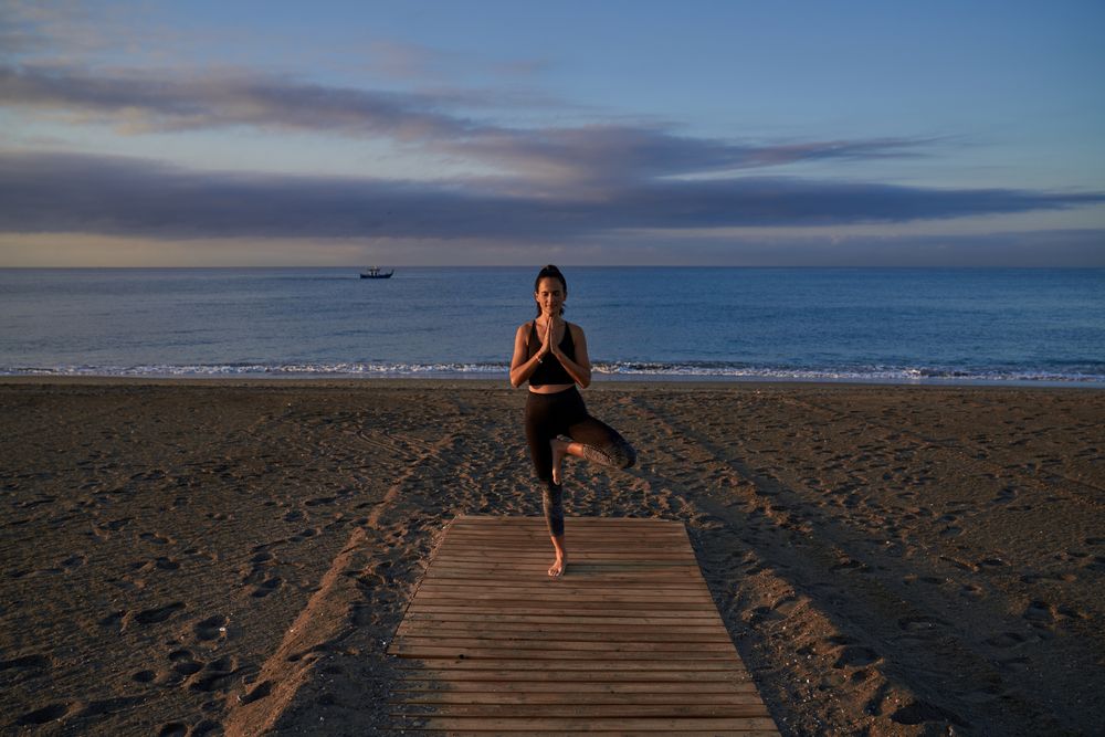 Hispanic woman practicing Tree pose on shore